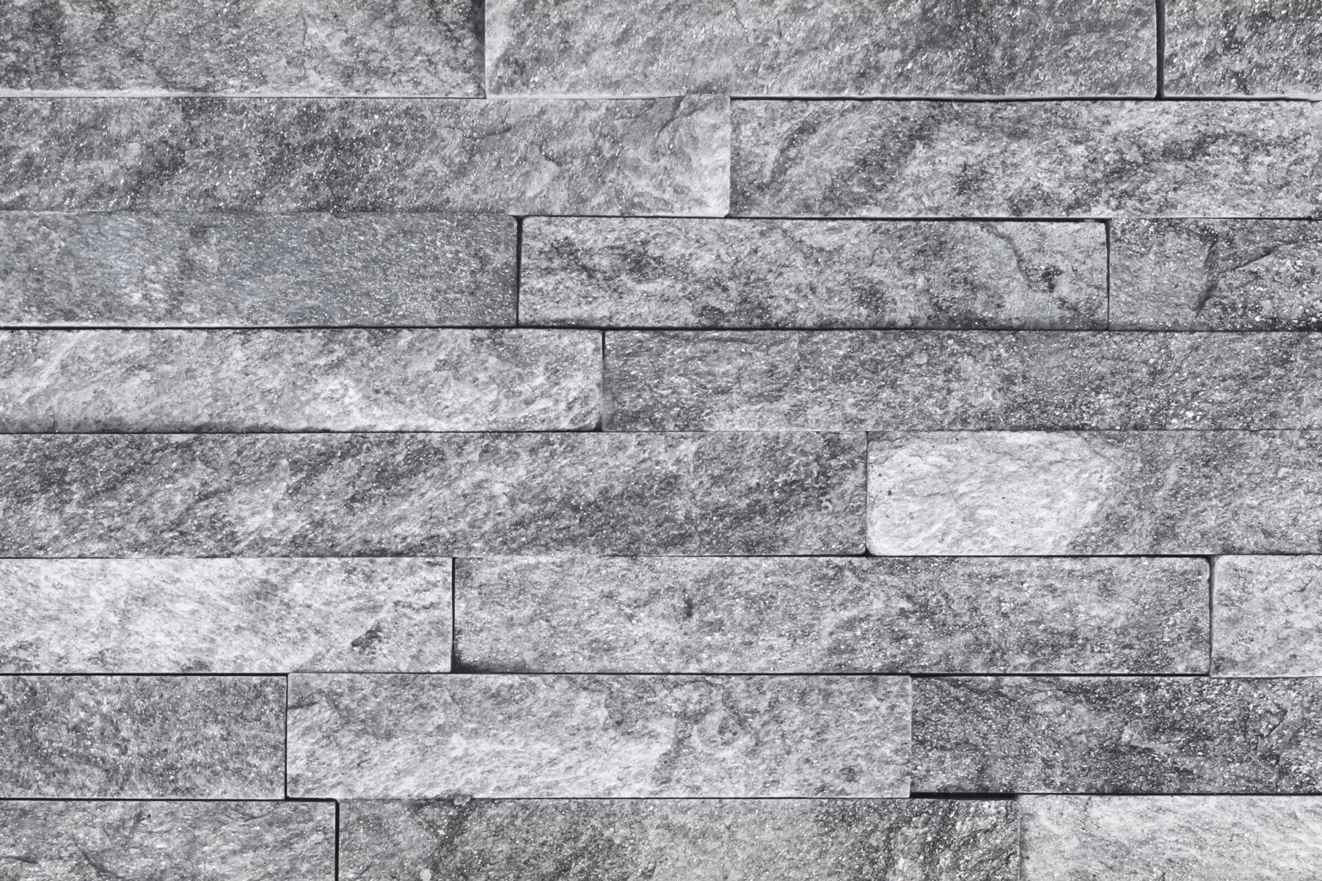 The image shows a wall with a pattern of rectangular gray stone tiles, arranged in an offset brick layout, with a textured surface.